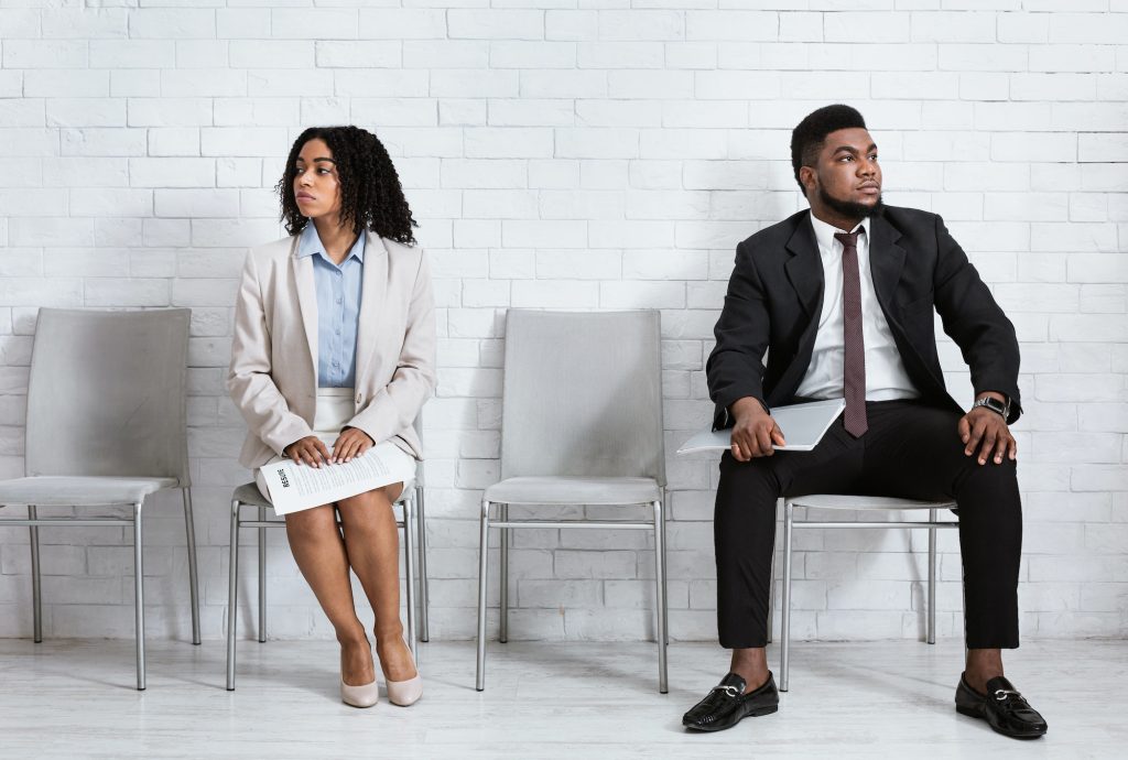 Black man and woman looking in opposite directions, feeling competitive while waiting for job