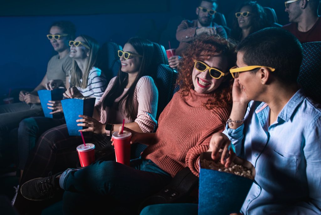 Group of cheerful people laughing while watching movie in cinema with 3D glasses.